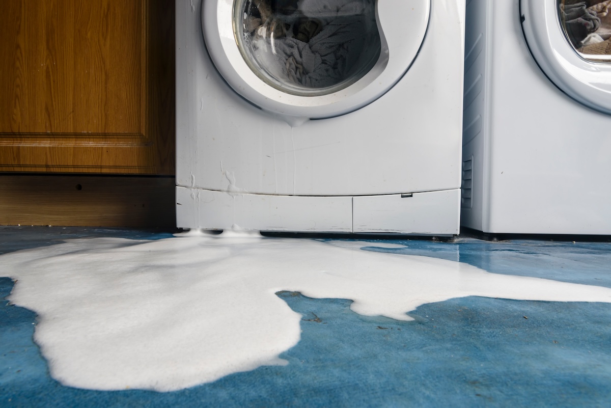 Soap bubbles pour out of a leaking washing machine.